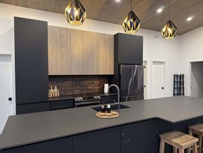 Une cuisine moderne dotée d’un grand îlot central, d’appareils électroménagers en acier inoxydable et de luminaires suspendus.