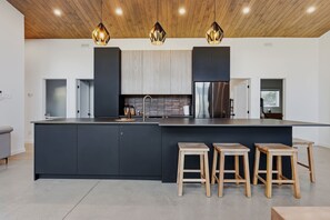 A modern kitchen with a large island, wooden stools, and pendant lighting.
