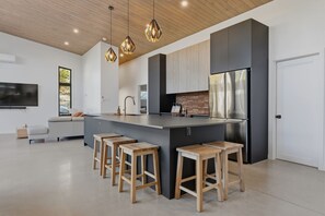 A modern kitchen with a central island, bar stools, a stainless steel refrigerator, and pendant lighting.