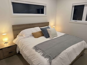 A neatly made bed with pillows, a bedside lamp, and a window above it. - Spa & Nature | Asini-Nibi (Ferme-Neuve)