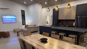 A modern kitchen with a central island, wooden dining table, and bar stools.