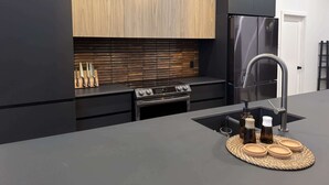 A modern kitchen with black cabinetry, a stainless steel refrigerator, a gas stove, and a sink with a faucet.