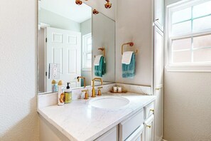 Un bagno con lavabo in marmo bianco, rubinetti dorati, uno specchio grande e una finestra con vista.