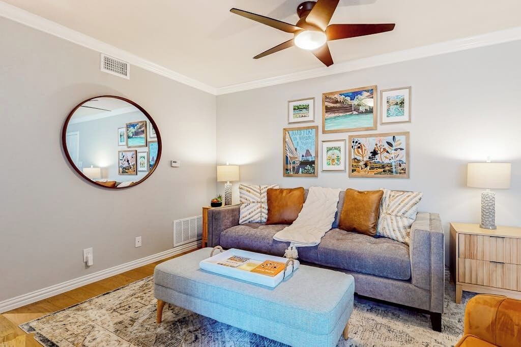 A living room with a grey sofa, a round mirror, and framed pictures on the wall.