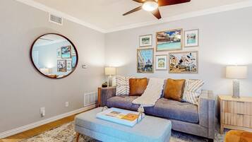 A living room with a grey sofa, a round mirror, and framed pictures on the wall.