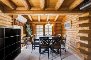 A log cabin interior with a dining table, chairs, a black entertainment unit, and a large window. - Stay in this unique Mountain Retreat "Cougar Lodge", nestled in the shadow of color-soaked San Jacinto mountains. Our cabin is just a short drive to town center. Spacious 5-bedroom log cabin with two living rooms and a huge game area with Pool Table, (Idyllwild)