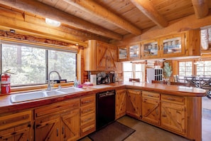 A wooden cabin kitchen with a large window, wooden cabinets, a dishwasher, and a sink. - Stay in this unique Mountain Retreat "Cougar Lodge", nestled in the shadow of color-soaked San Jacinto mountains. Our cabin is just a short drive to town center. Spacious 5-bedroom log cabin with two living rooms and a huge game area with Pool Table, (Idyllwild)