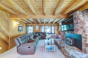 A log cabin interior with a stone fireplace, wooden beams, a leather sofa, and a large window. - Stay in this unique Mountain Retreat "Cougar Lodge", nestled in the shadow of color-soaked San Jacinto mountains. Our cabin is just a short drive to town center. Spacious 5-bedroom log cabin with two living rooms and a huge game area with Pool Table, (Idyllwild)