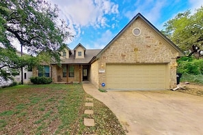 A two-story house with a stone facade, a garage, and a front yard with a pathway. - Scenic retreat with fenced yard, patio, central AC, & washer/dryer (Austin)