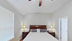 Ein Schlafzimmer mit einem großen Bett, zwei Nachttischen mit Lampen, einem Deckenventilator und einer Tür.