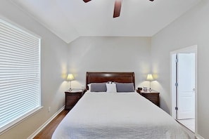 A bedroom with a large bed, two bedside tables with lamps, a ceiling fan, and a door. - Scenic retreat with fenced yard, patio, central AC, & washer/dryer (Austin)