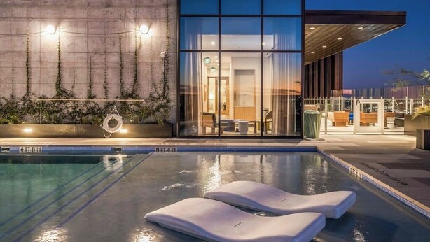 En moderne bygning med swimmingpool, liggestole og en glasfacade.