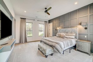 Ein Schlafzimmer mit Bett, Deckenventilator, Fernseher und einem Fenster mit Vorhängen.