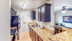 A kitchen with granite countertops, dark cabinets, a built-in stove, and a ceiling fan. - Lovely Austin condo close to downtown with streaming, W/D, central AC, & WiFi (Austin)
