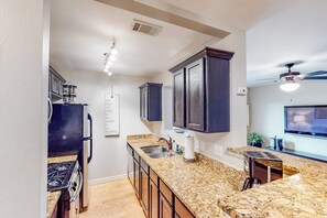 A kitchen with granite countertops, dark cabinets, a built-in stove, and a ceiling fan.