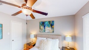 A bedroom with a bed, two bedside tables with lamps, a ceiling fan, a door, and a painting on the wall. - Lovely Austin condo close to downtown with streaming, W/D, central AC, & WiFi (Austin)