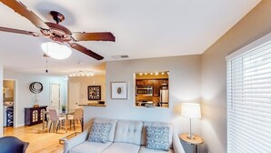 A modern living room with a sofa, dining area, ceiling fan, and kitchen in the background. - Lovely Austin condo close to downtown with streaming, W/D, central AC, & WiFi (Austin)