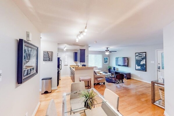 A modern living room with a dining area, a kitchen, and a TV mounted on the wall.