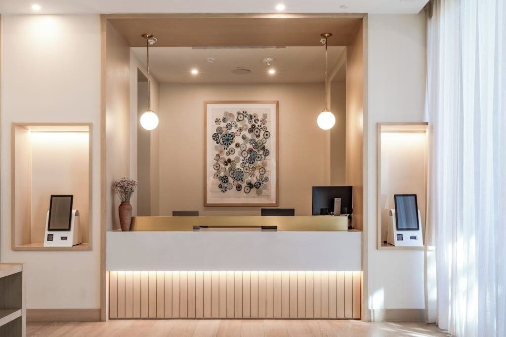 Bancada de recepção com uma obra de arte abstrata emoldurada, dois totens digitais e um painel de madeira.