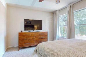 Ein Schlafzimmer mit einem Bett, einer Holzkommode, einem Flachbildfernseher und einem Fenster mit Vorhängen.