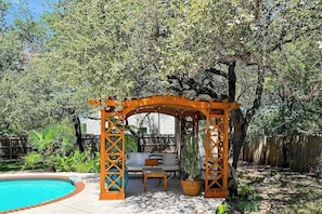 Ein überdachter Patio-Bereich mit Pool, Gartenmöbeln und einer Holz-Pergola.