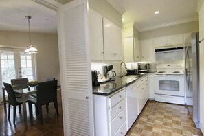 A modern kitchen with white cabinets, a dining area with a table and chairs, and a built-in oven and refrigerator.