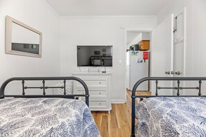 Ein Schlafzimmer mit zwei Betten, einem Schminktisch, einem Fernseher und einer Tür zu einer Küche.