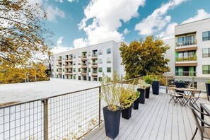 Terraço no telhado com plantas em vasos, móveis de exterior e vista para edifícios modernos.