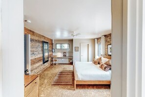 Quarto com cama de madeira, escrivaninha, cadeira e ventilador de teto.