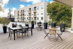 Eine Dachterrasse mit Tisch und Stühlen, Blumentöpfen und einem modernen Gebäude im Hintergrund.