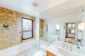 Uma casa de banho com parede de tijolo, um espelho grande, uma banheira e uma pia moderna.