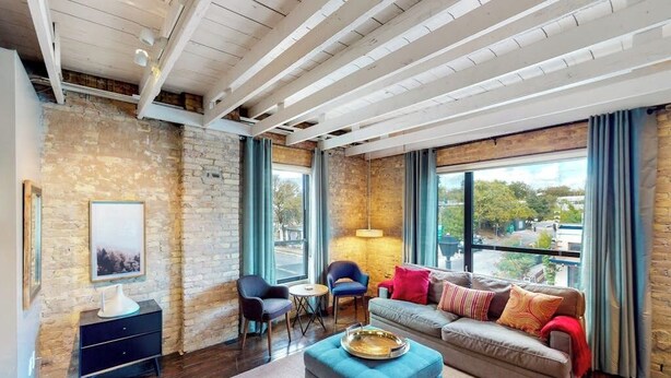 Una sala de estar moderna con pared de piedra, ventanas amplias, un sofá, una mesa de centro y una lámpara.