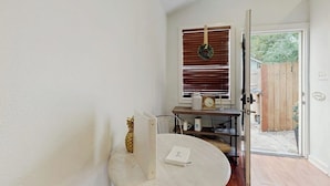 Une pièce avec une porte blanche, un cadre de porte en bois, un mur blanc, un plancher en bois, une table blanche, une chaise blanche, une étagère blanche, une horloge blanche, un vase blanc, une clôture en bois et un portail en bois.