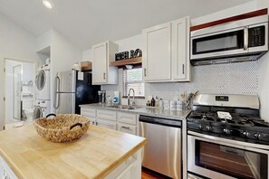 Una cocina moderna con armarios blancos, un refrigerador de acero inoxidable, un microondas, una estufa y un lavavajillas.