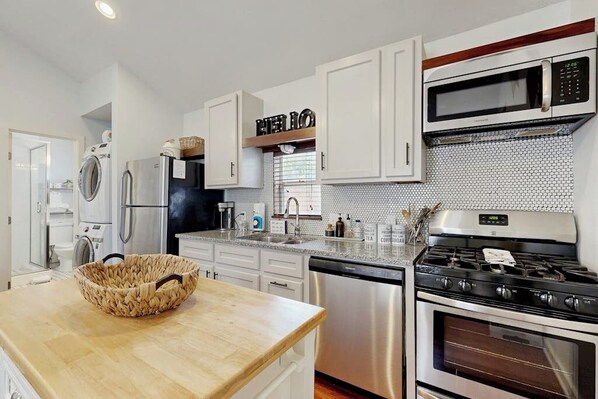A modern kitchen with white cabinets, a stainless steel refrigerator, a microwave, a stove, and a dishwasher.