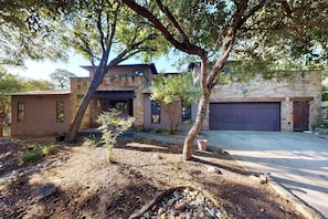 A modern house with a stone facade, a garage, and a landscaped yard with trees and shrubs. - Charming home with balcony, firepit, & 2 living rooms - near dining & music (Austin)