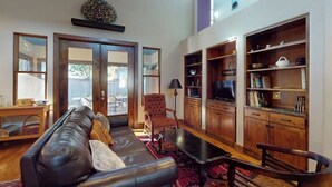 Un salon avec un canapé en cuir, une table basse en bois, un tapis rouge, une bibliothèque en bois et un téléviseur.
