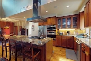 A modern kitchen with a central island, stainless steel appliances, wooden cabinets, and a dining area with chairs. - Charming home with balcony, firepit, & 2 living rooms - near dining & music (Austin)