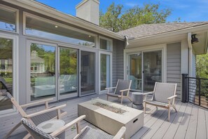 Eine Terrasse mit Gartenmöbeln, einer Feuerstelle und großen Schiebeglasüren.