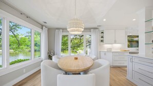 Une cuisine moderne avec une table ronde en bois, des meubles blancs et de grandes fenêtres donnant sur un paysage verdoyant.