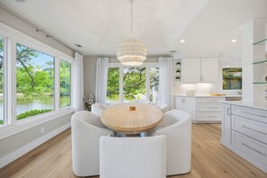 Eine moderne Küche mit einem runden Holztisch, weißen Schränken und großen Fenstern mit Blick ins Grüne.