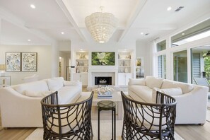 Ein modernes Wohnzimmer mit weißen Sofas, einem Kamin und einer großen Chandelier.