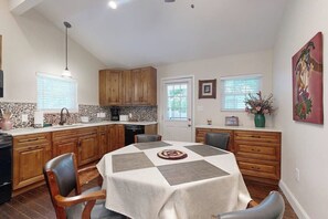 Una cocina con mesa de comedor, armarios de madera, salpicadero de piedra y una ventana con persianas.