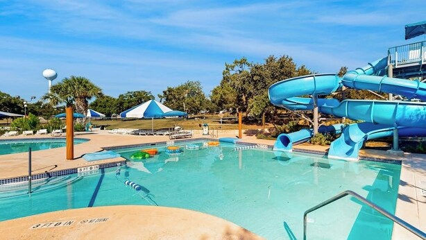 A pool area with a water slide, lounge chairs, and a palm tree. - Stylish Hideaway w/ Chic Kitchen & Private Patio - Located at World of Tennis (Lakeway)