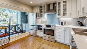 A modern kitchen with white cabinetry, stainless steel appliances, and a large window overlooking a deck. - Stylish Hideaway w/ Chic Kitchen & Private Patio - Located at World of Tennis (Lakeway)