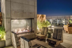 A modern outdoor seating area with a fire feature, wooden furniture, and a city view at dusk. - 13th floor corner condo, lake-view balcony, rooftop pool & gym, dog-friendly (Austin)