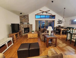 Un salon spacieux doté d’une cheminée, de meubles en bois, d’un téléviseur et d’un coin repas avec des chaises et une table.