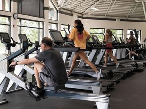 Ein Fitnessraum mit mehreren Laufbändern, einem Rudergerät und einer Person, die das Rudergerät benutzt.