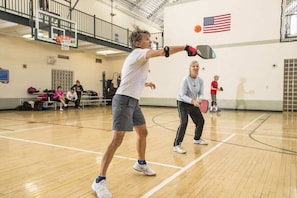 Eine Sporthalle mit einem Basketballkorb, einer Flagge und Personen bei sportlichen Aktivitäten.