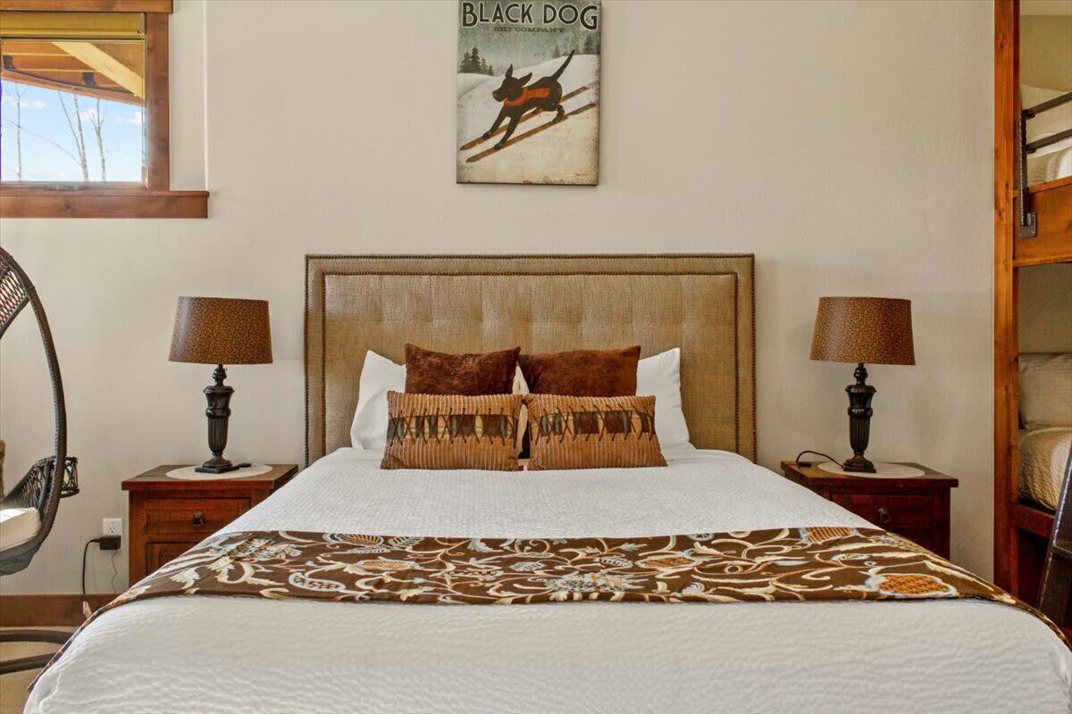 A bedroom with a large bed, two bedside tables with lamps, a headboard, and a wall-mounted poster of a dog.